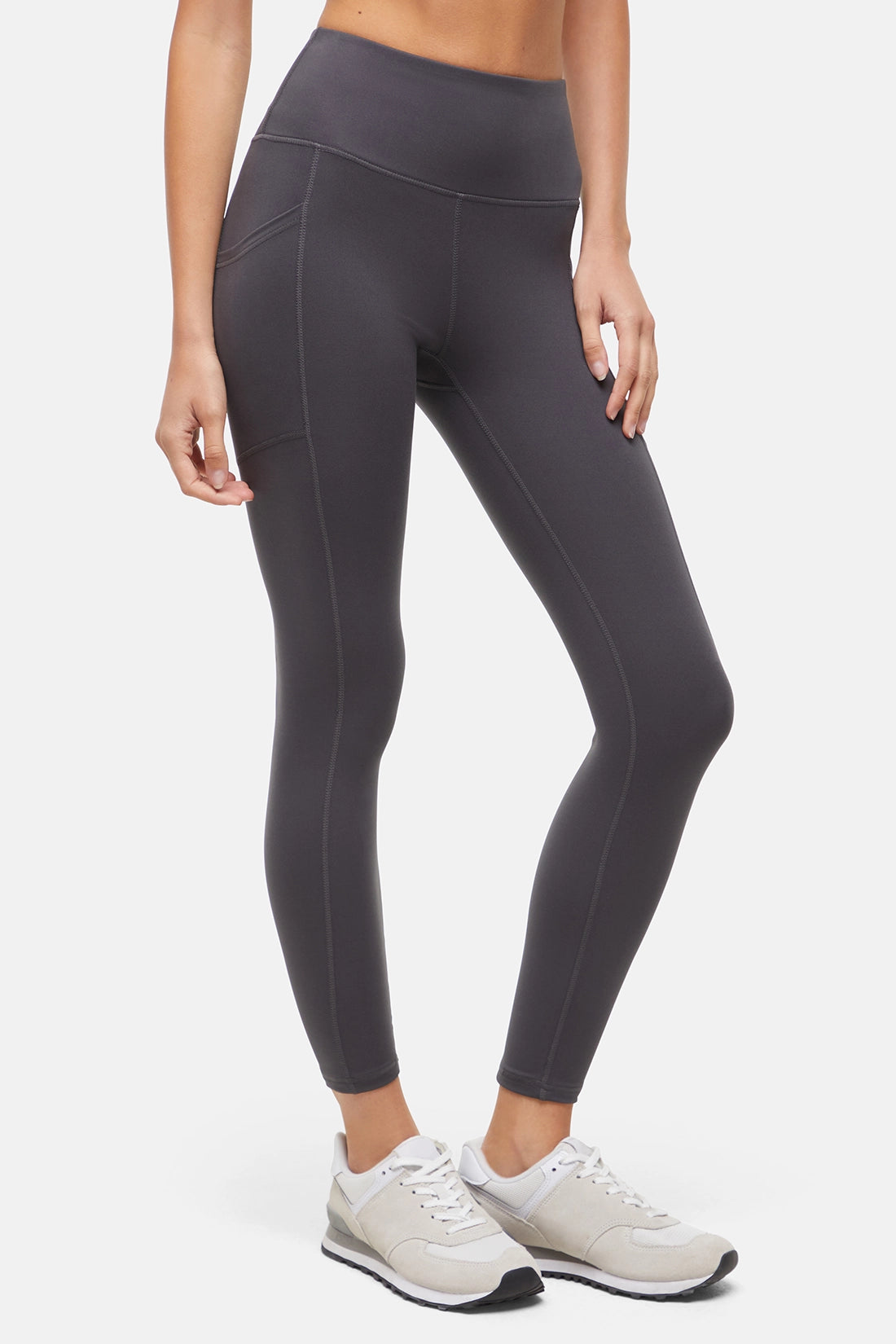 Front view of woman wearing dark gray leggings with a white background. 
