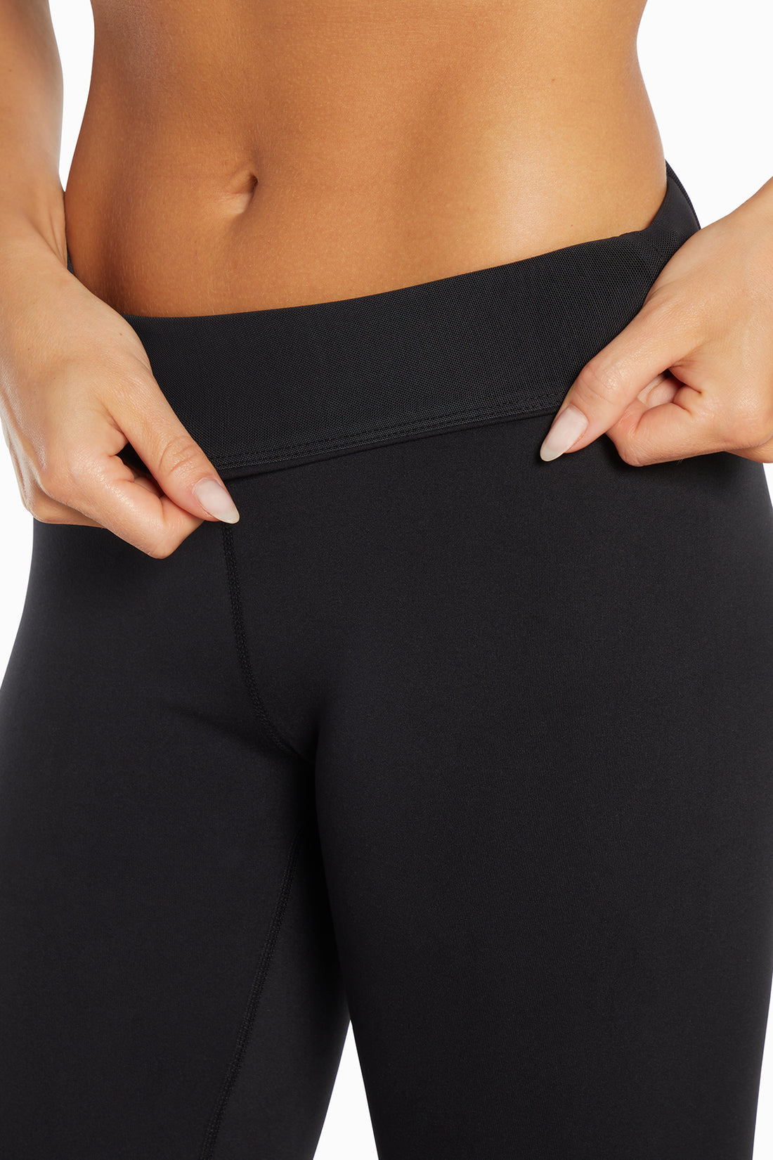 Close up of view of woman wearing black leggings and showing inner mesh waistband on a white background. 