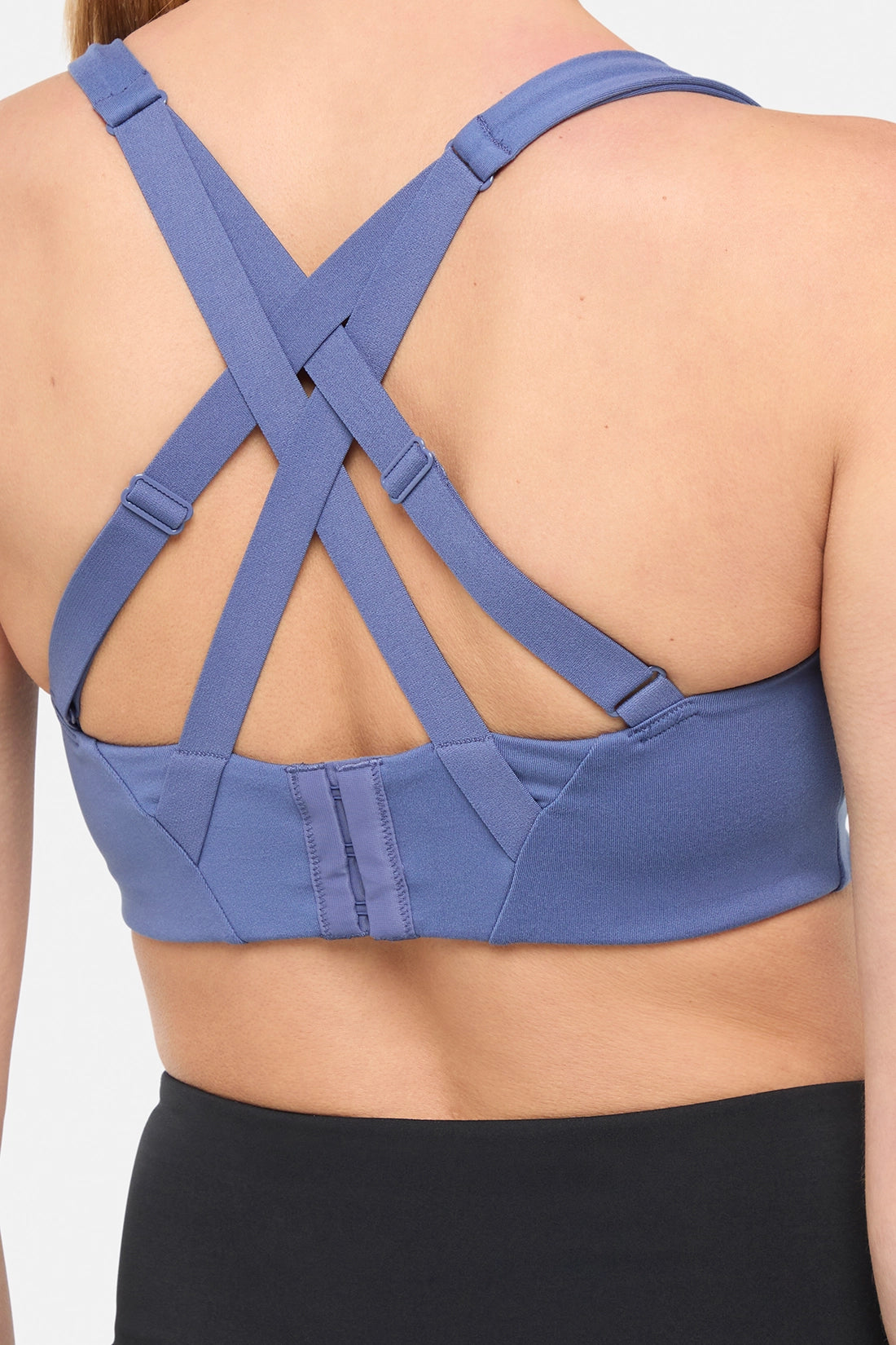 Close up back view of blue sports bra with strappy crisscross straps on a plain background. 