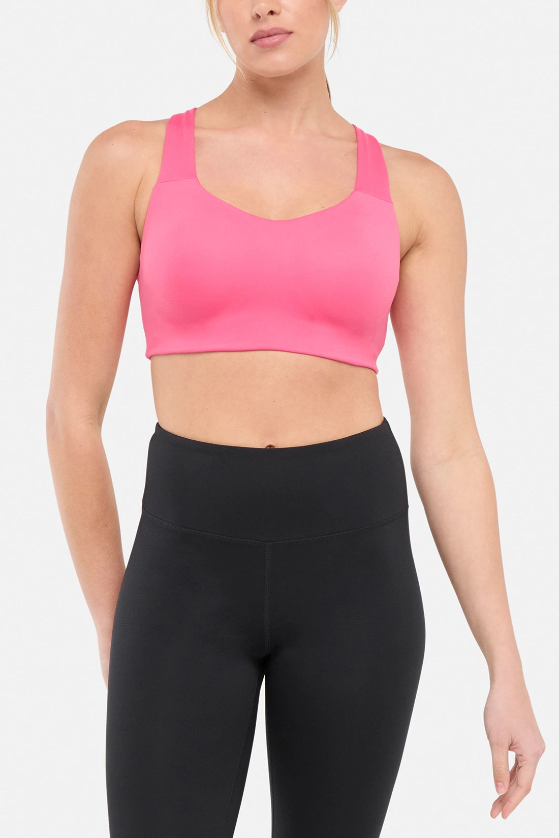 Front view of woman wearing a pink sports bra and black leggings on a white background.