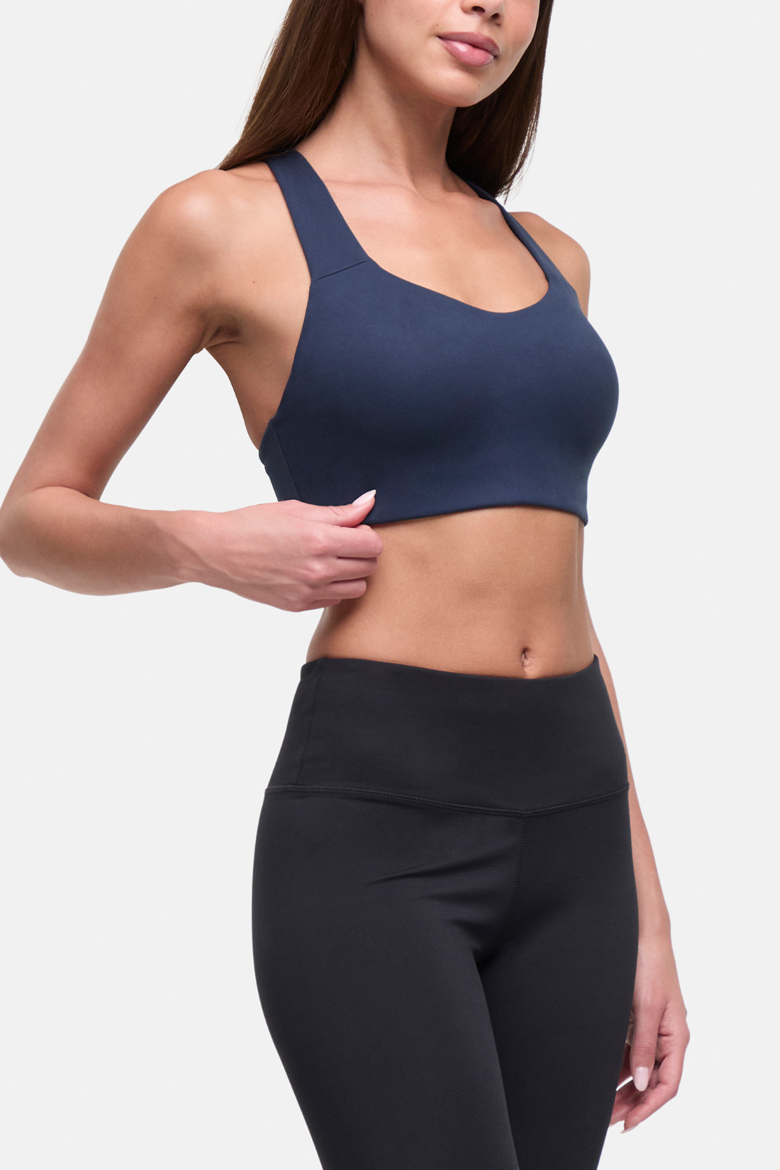 A woman wearing a navy blue sports bra and black high-waisted leggings, shown from the chest down against a light gray studio background. 
