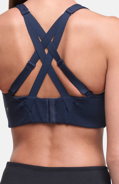 Back view of a navy blue sports bra with crisscrossing shoulder straps and a center back strap, shown on a model. 