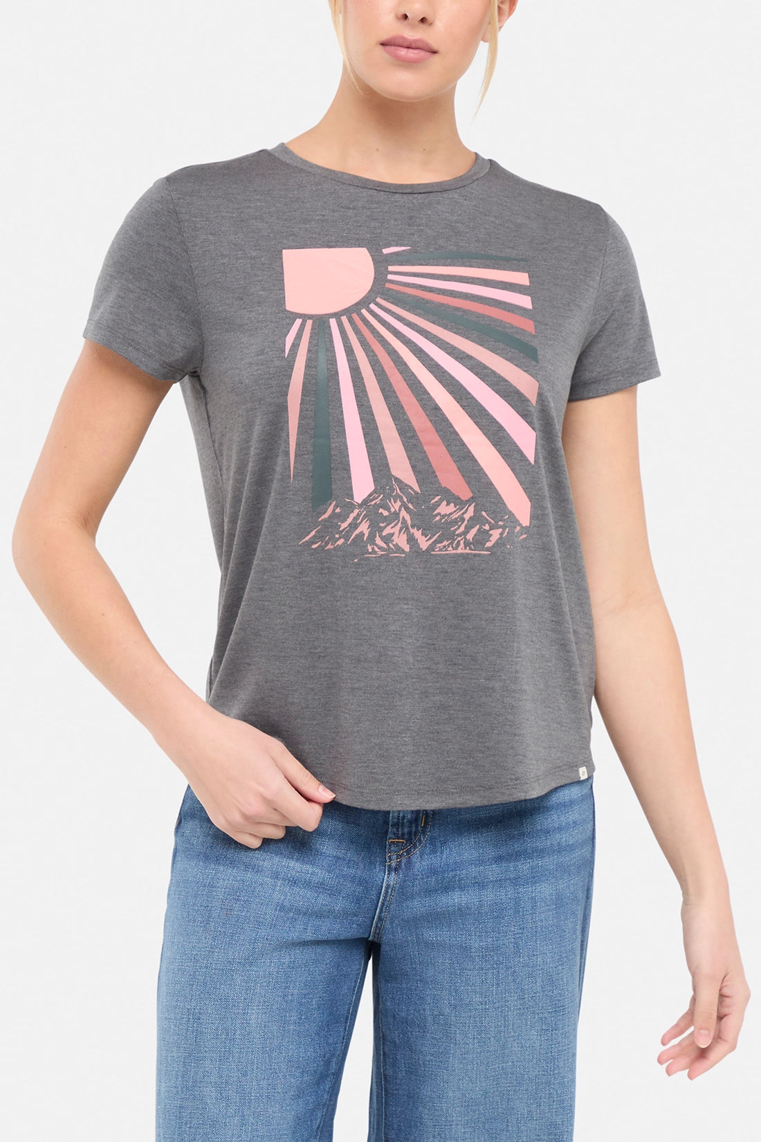 Front view of woman wearing a gray t-shirt with a pink sun and mountain graphic on a white background. 