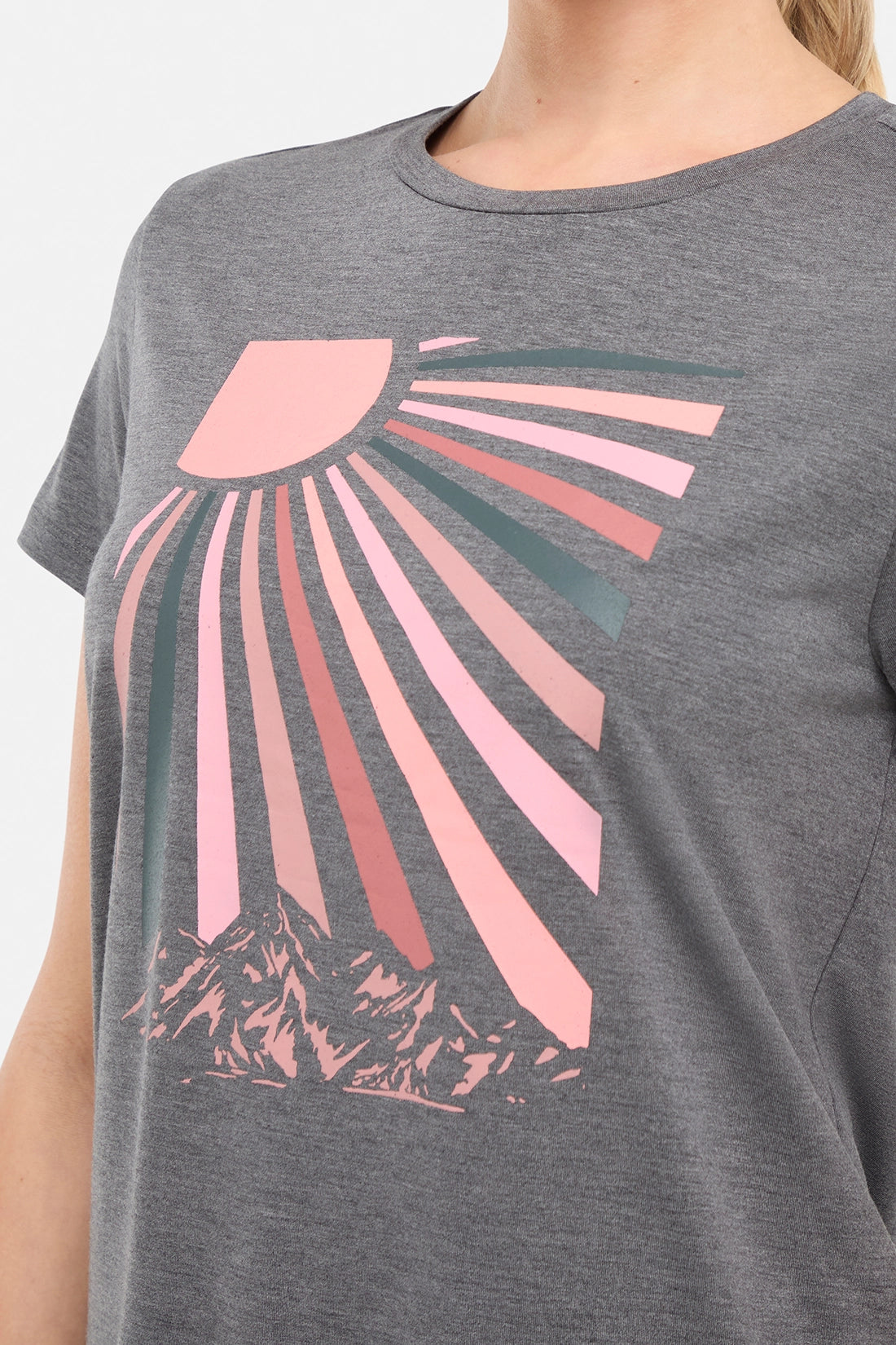 Close up front view of woman wearing a gray t-shirt with a pink sun and mountain graphic on a white background. 