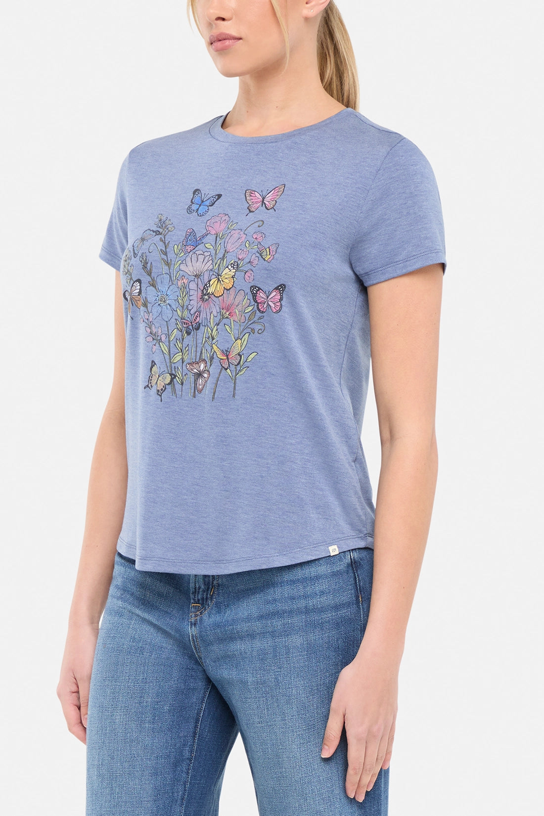 Side view of woman wearing a blue t-shirt with butterflies and floral design on a white background. 