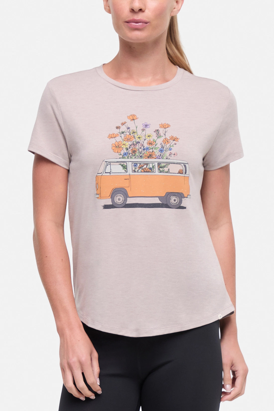 Front view of woman wearing a beige t-shirt with a graphic of an orange van and flowers on a .white background. 