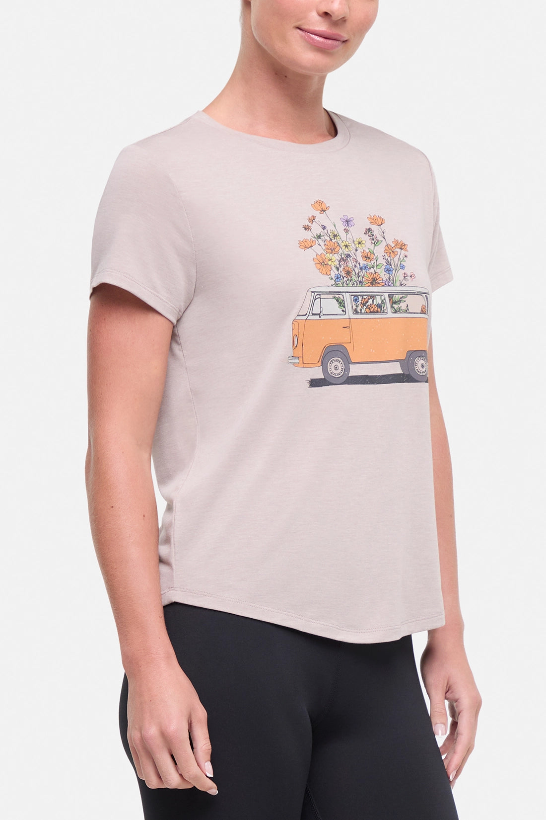 Front view of woman wearing a beige t-shirt with a graphic of an orange van and flowers on a .white background. 