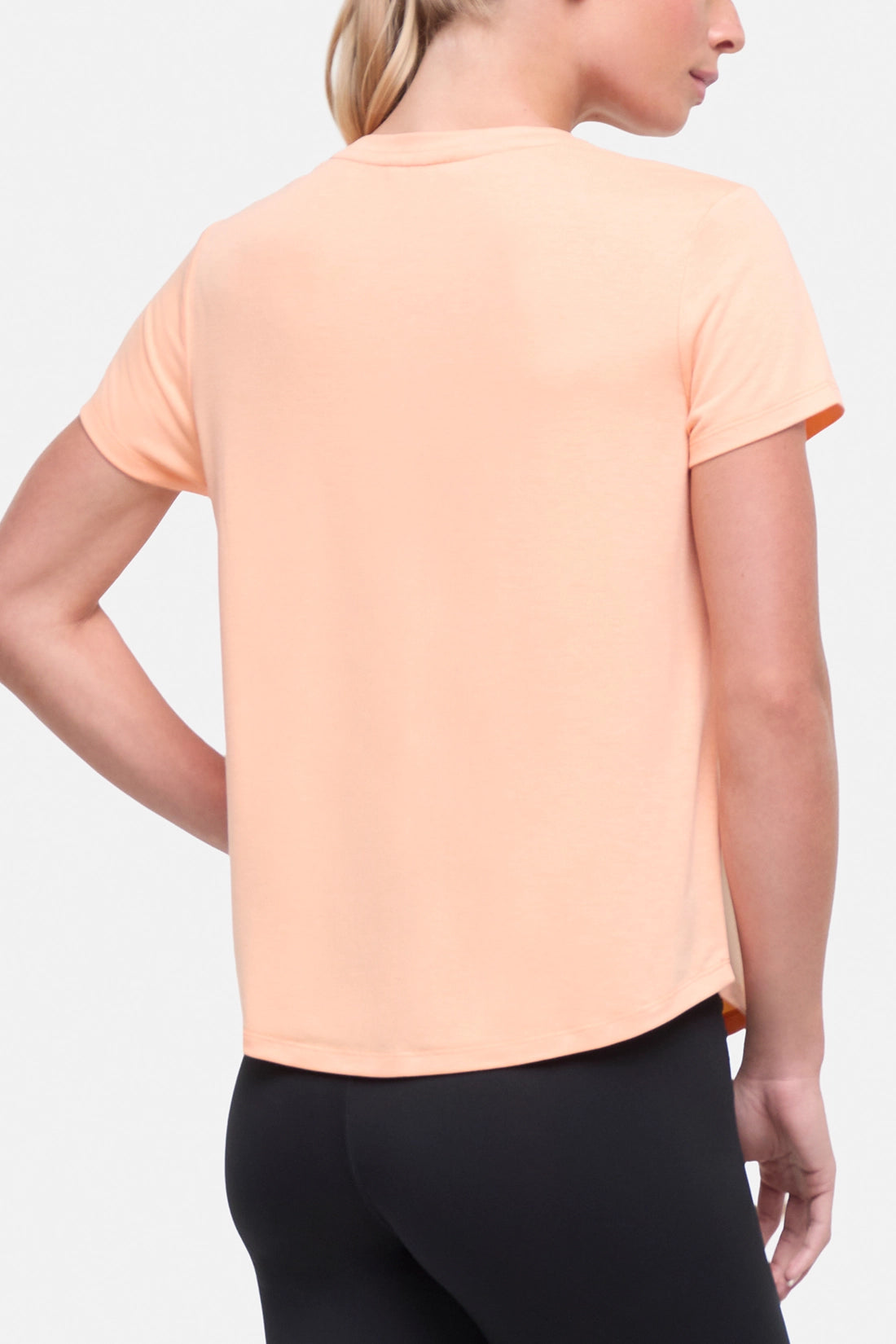 Back view of woman wearing a peach t-shirt with floral graphic on a light gray background. 