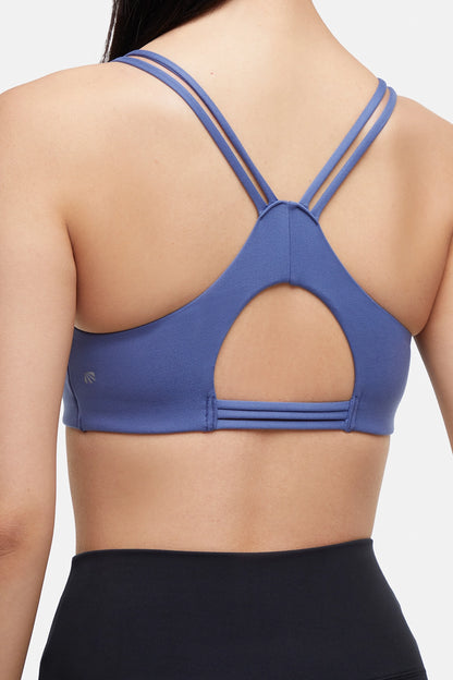 Close up back view of blue sports bra with crisscross straps and keyhole cutout detail on a plain background. 