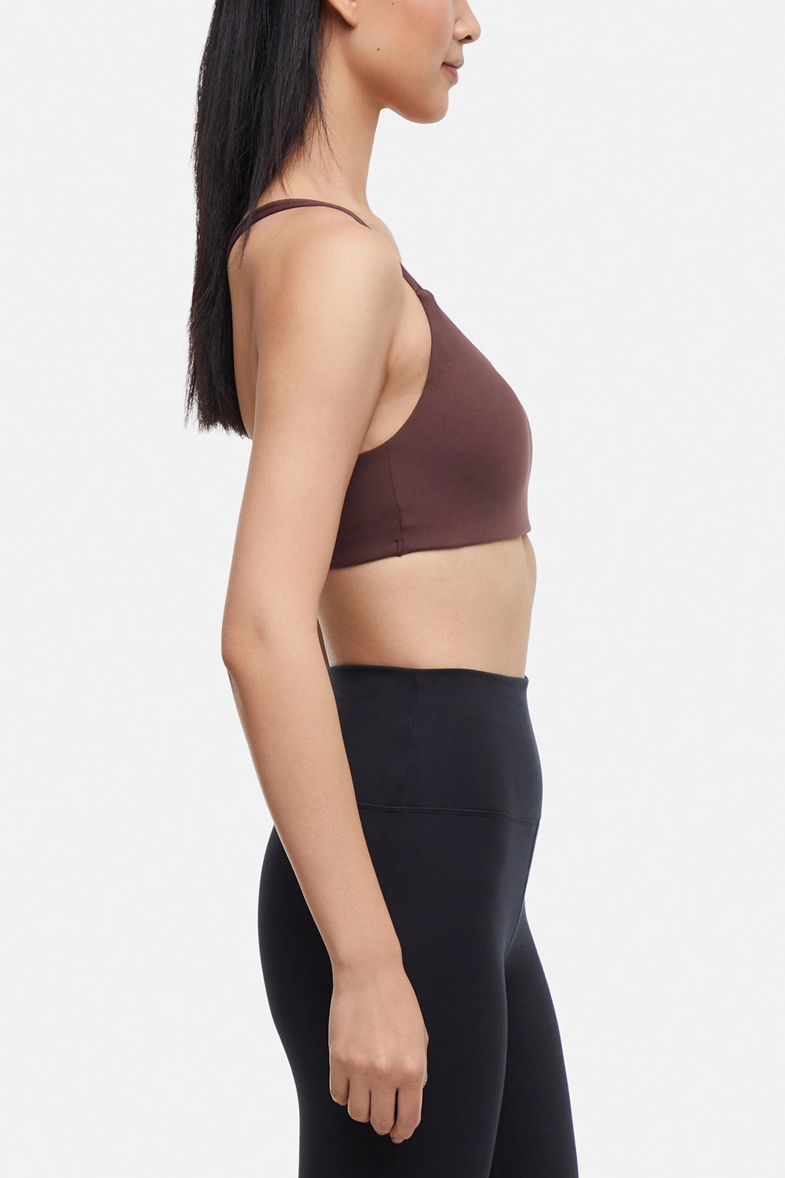 Side view of woman wearing a brown sports bra and black leggings on a white background. 