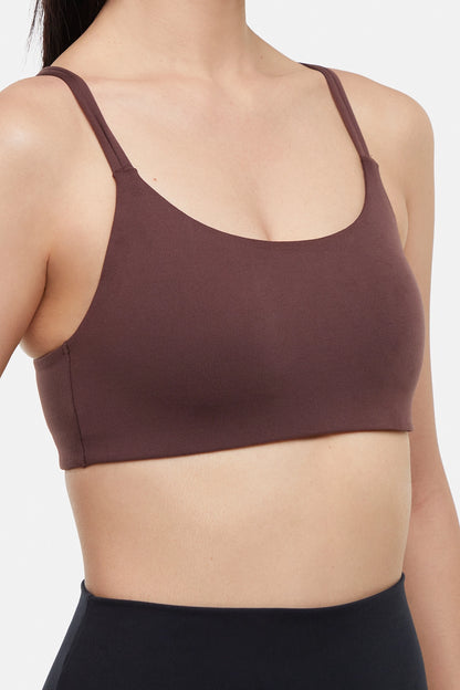 Close up front view of woman wearing a brown sports bra and black leggings on a white background. 