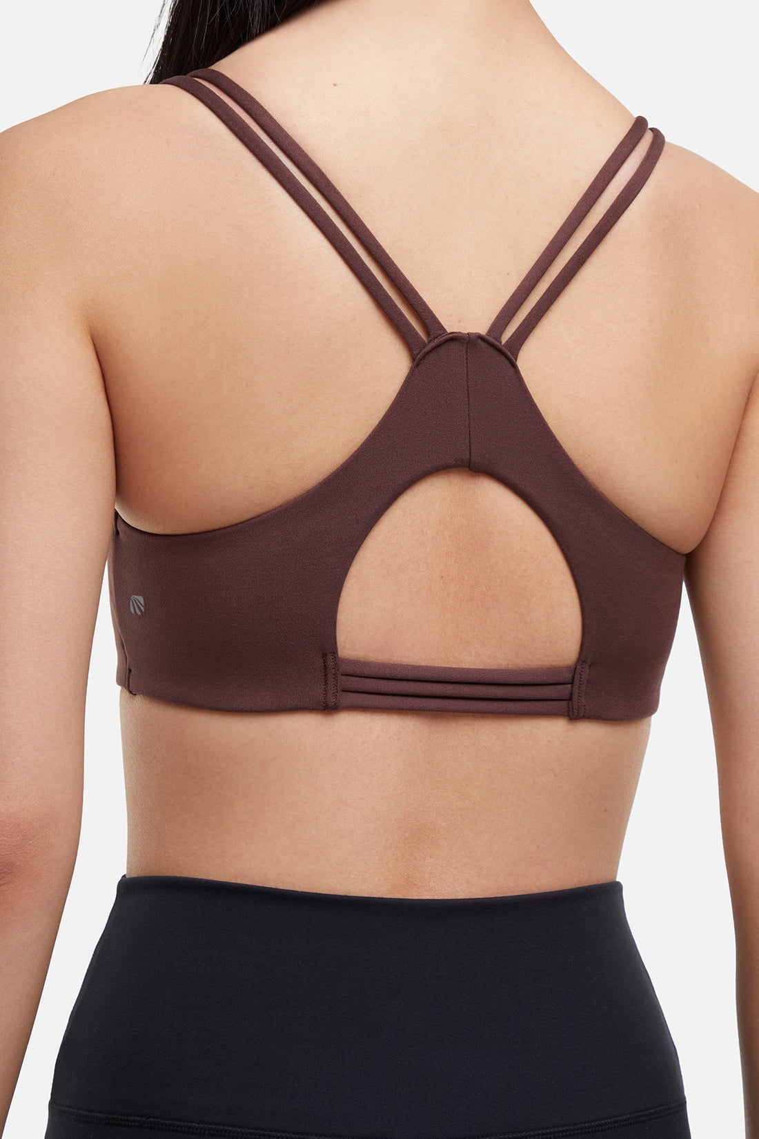 Close up back view of brown sports bra with crisscross straps and keyhole cutout detail on a plain background. 