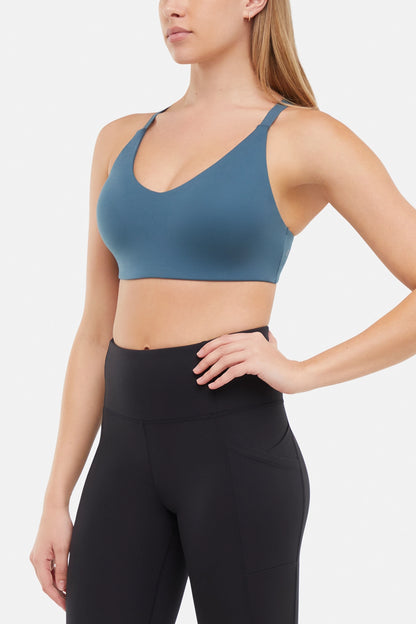Front view of woman wearing a blue sports bra and black leggings on a white background. 