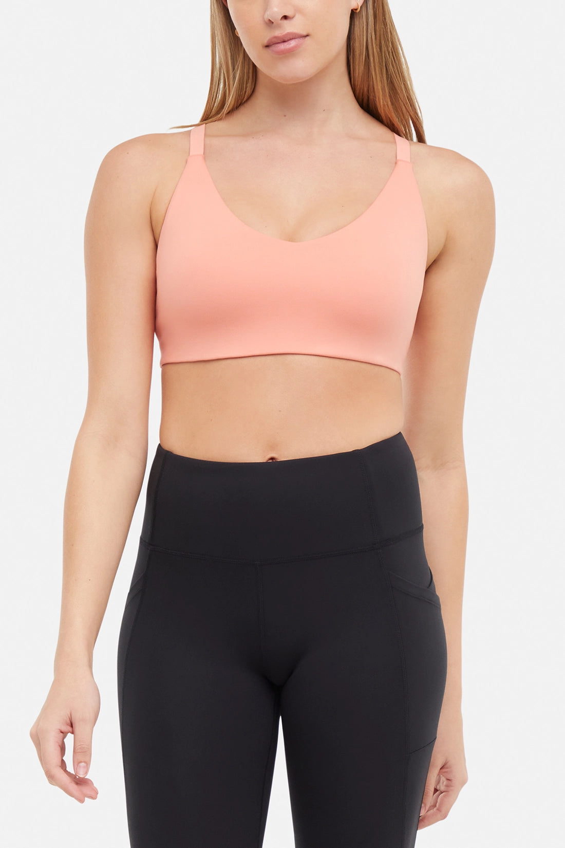 Front view of woman wearing a peach sports bra and black leggings on a white background.