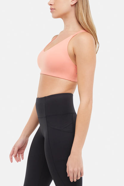 Side view of woman wearing a peach sports bra and black leggings on a white background. 