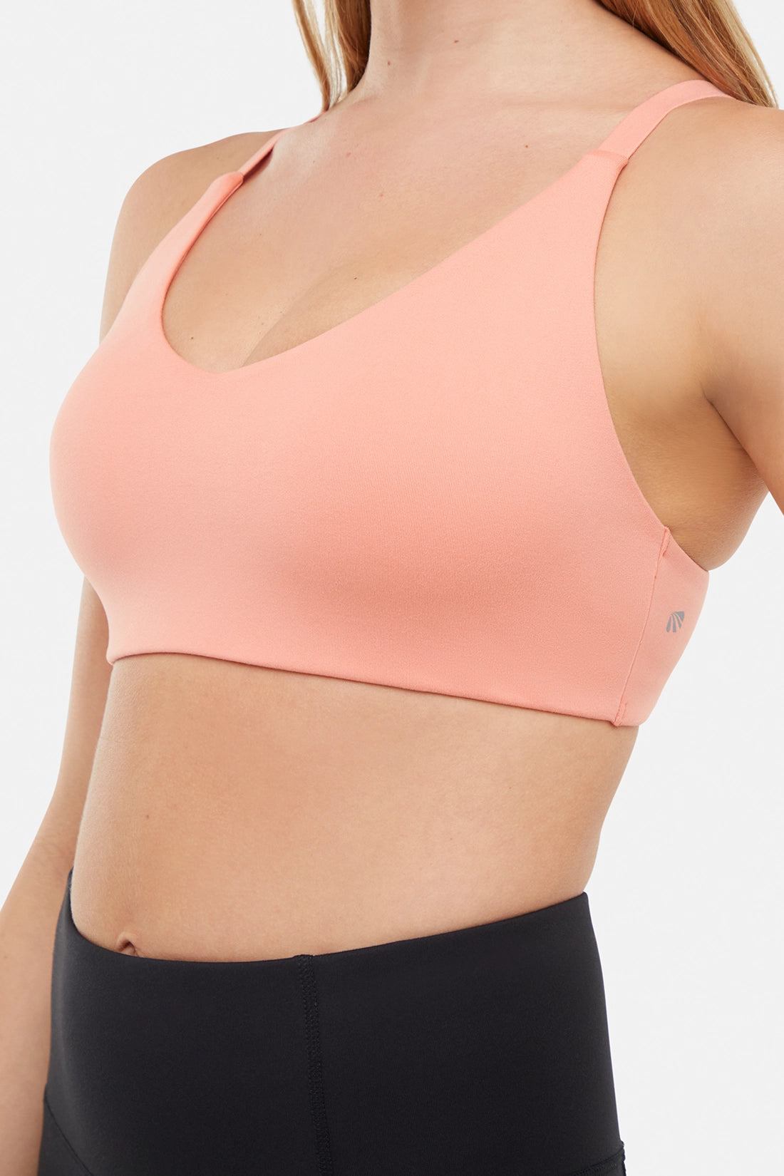 Close up front view of woman wearing a peach sports bra and black leggings on a white background. 