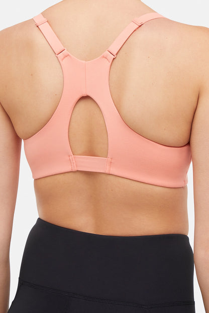Close up view of woman wearing a peach sports bra and black leggings on a white background. 