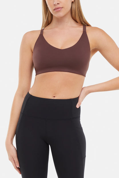 Front view of woman wearing a brown sports bra and black leggings on a white background. 