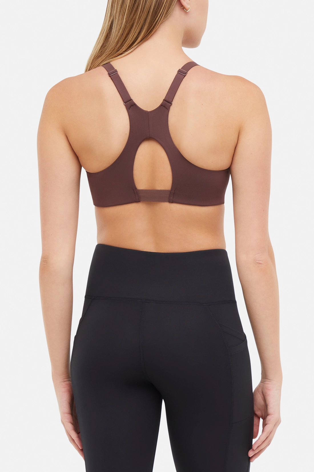 Back view of woman wearing a brown sports bra and black leggings on a white background. 