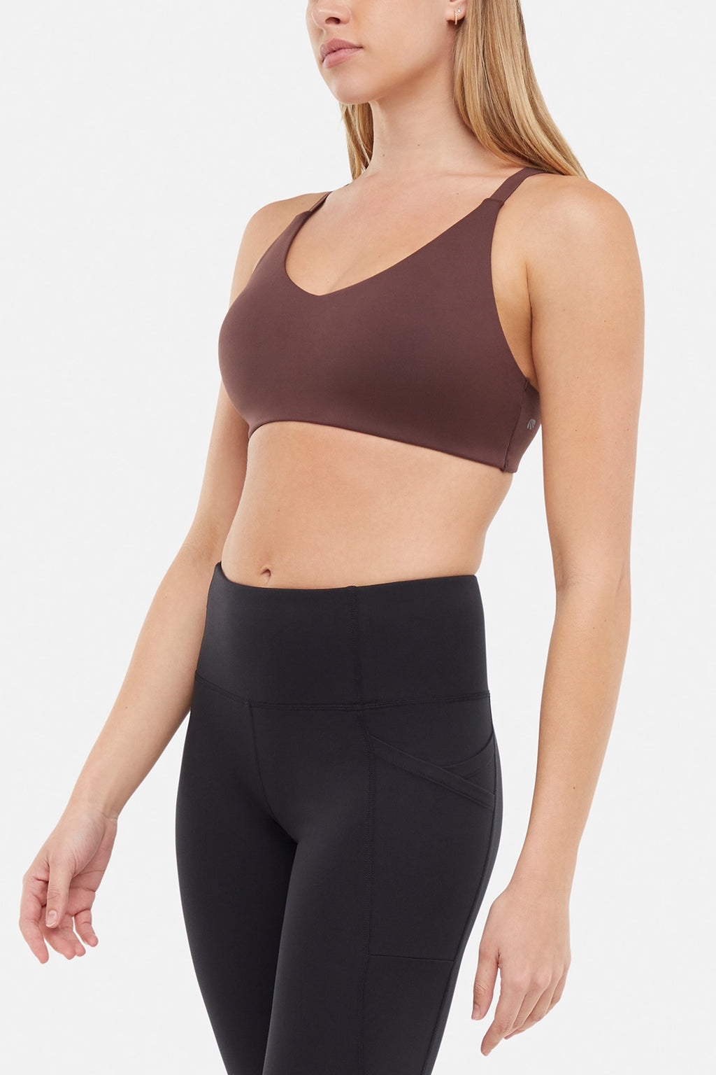 Side front view of woman wearing a brown sports bra and black leggings on a white background. #color_french-roast