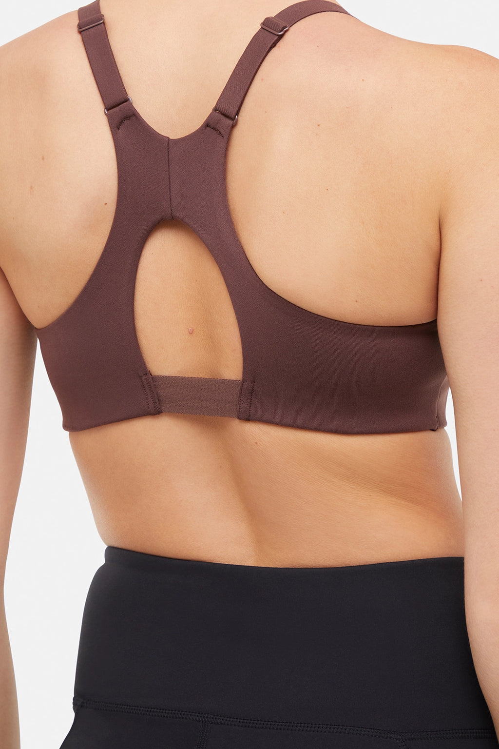 Close up back view of woman wearing a brown sports bra and black leggings on a white background. #color_french-roast