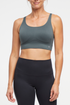 Front view of woman wearing a gray-green sports bra and black leggings on a white background. 
