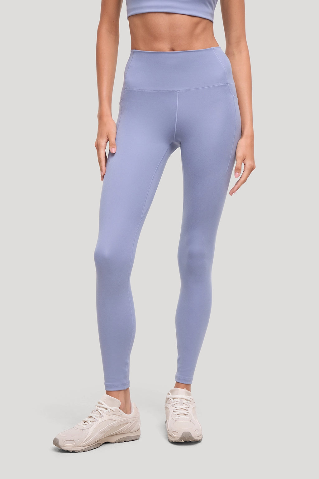 A model wearing high-waisted, light periwinkle blue leggings and beige sneakers, shown from the waist down against a solid light gray background. #color_tempest