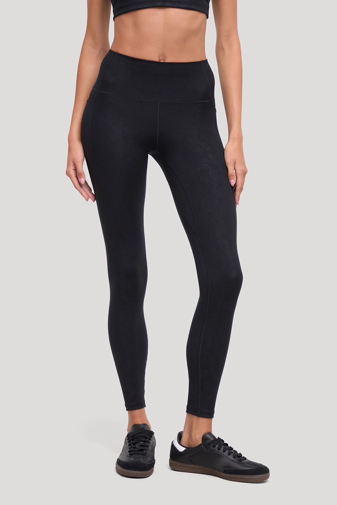 A model wearing black high-waisted leggings with all around animal camo print and black sneakers, shown from the waist down against a solid light gray background. #color_black-linear-animal-camo