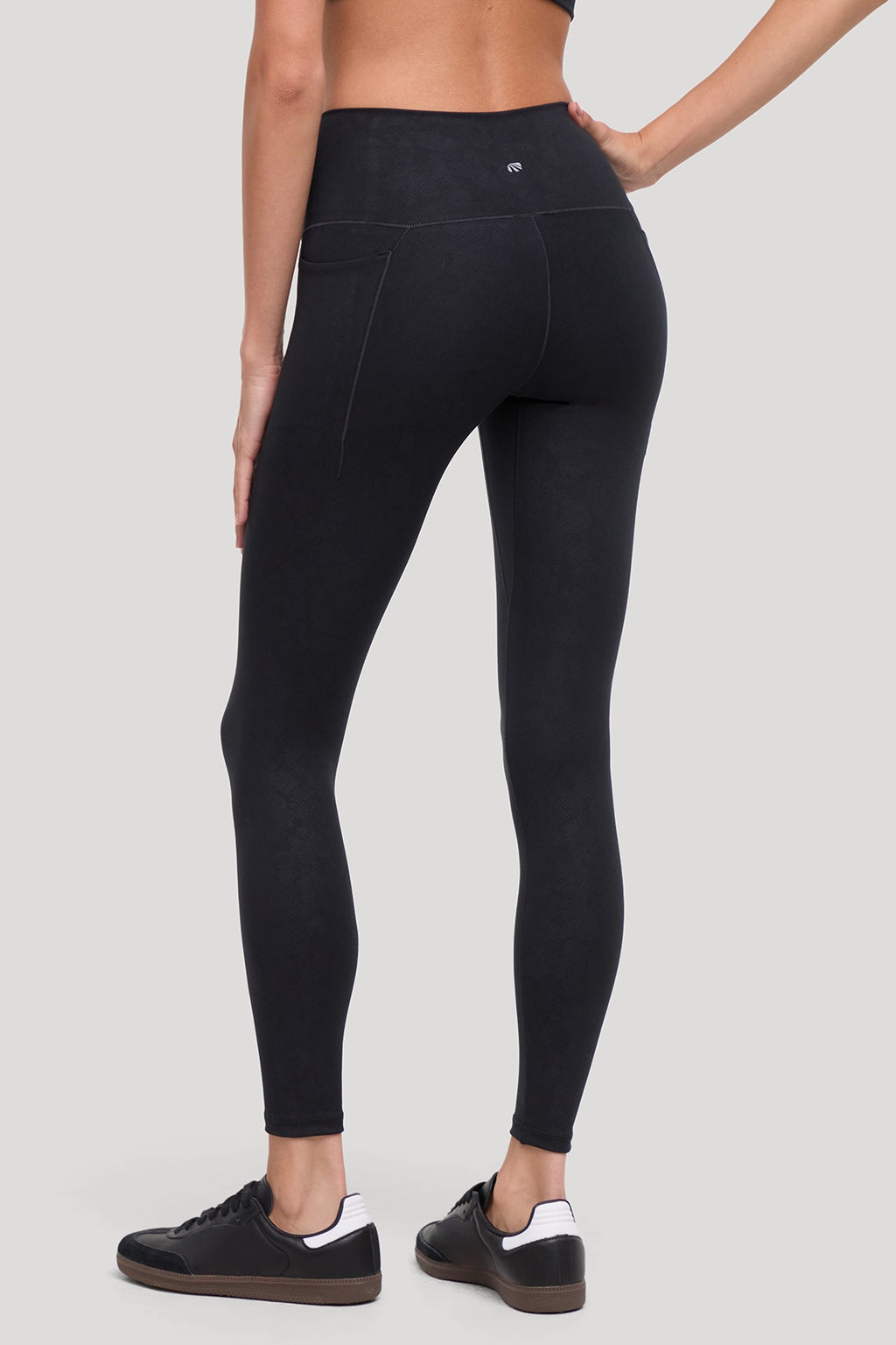 Rear view of a model wearing black high-waisted leggings with all around animal camo print  and with side pockets and black sneakers, set against a solid light gray background. #color_black-linear-animal-camo
