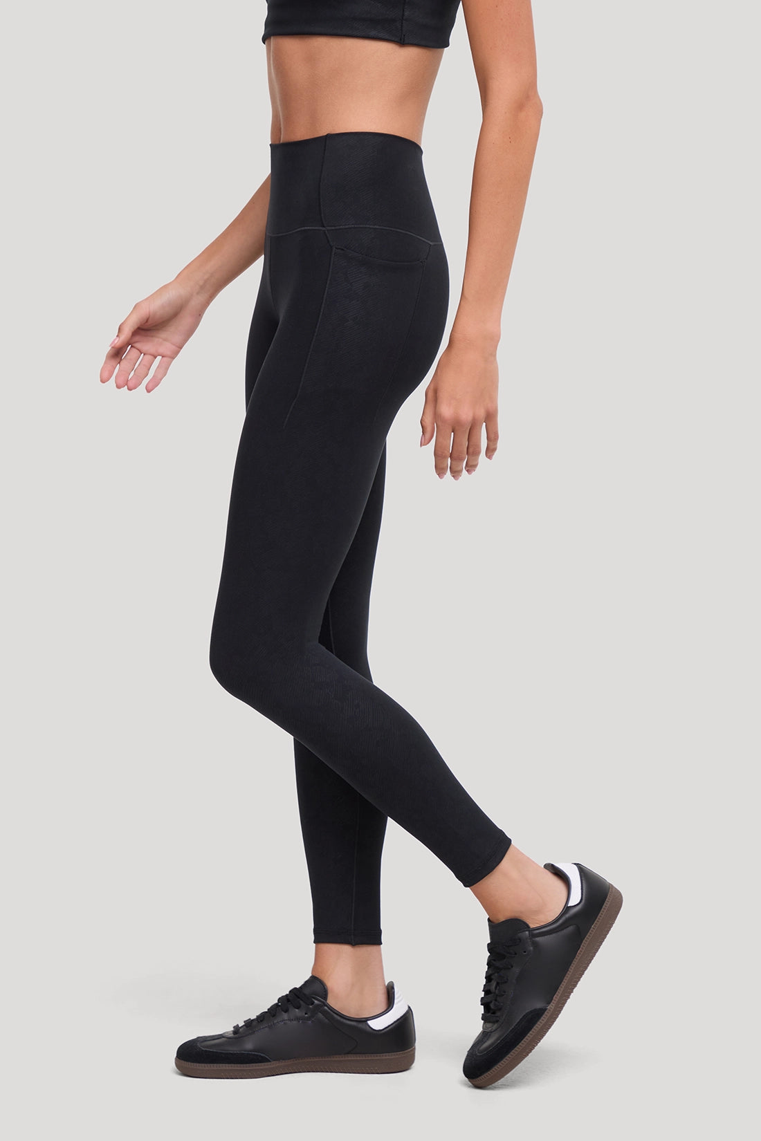 A model wearing black high-waisted leggings with all around animal camo print and black sneakers, shown from the waist down in a side-profile walking pose against a light gray studio background. #color_black-linear-animal-camo