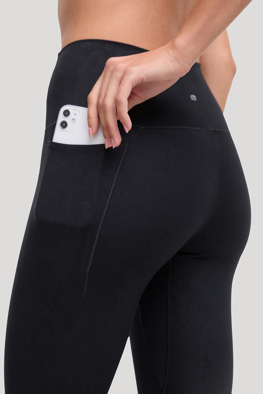 Close-up of a person wearing black high-waisted leggings with all around animal camo print and with a side pocket holding a white smartphone, shown against a light gray studio background. #color_black-linear-animal-camo