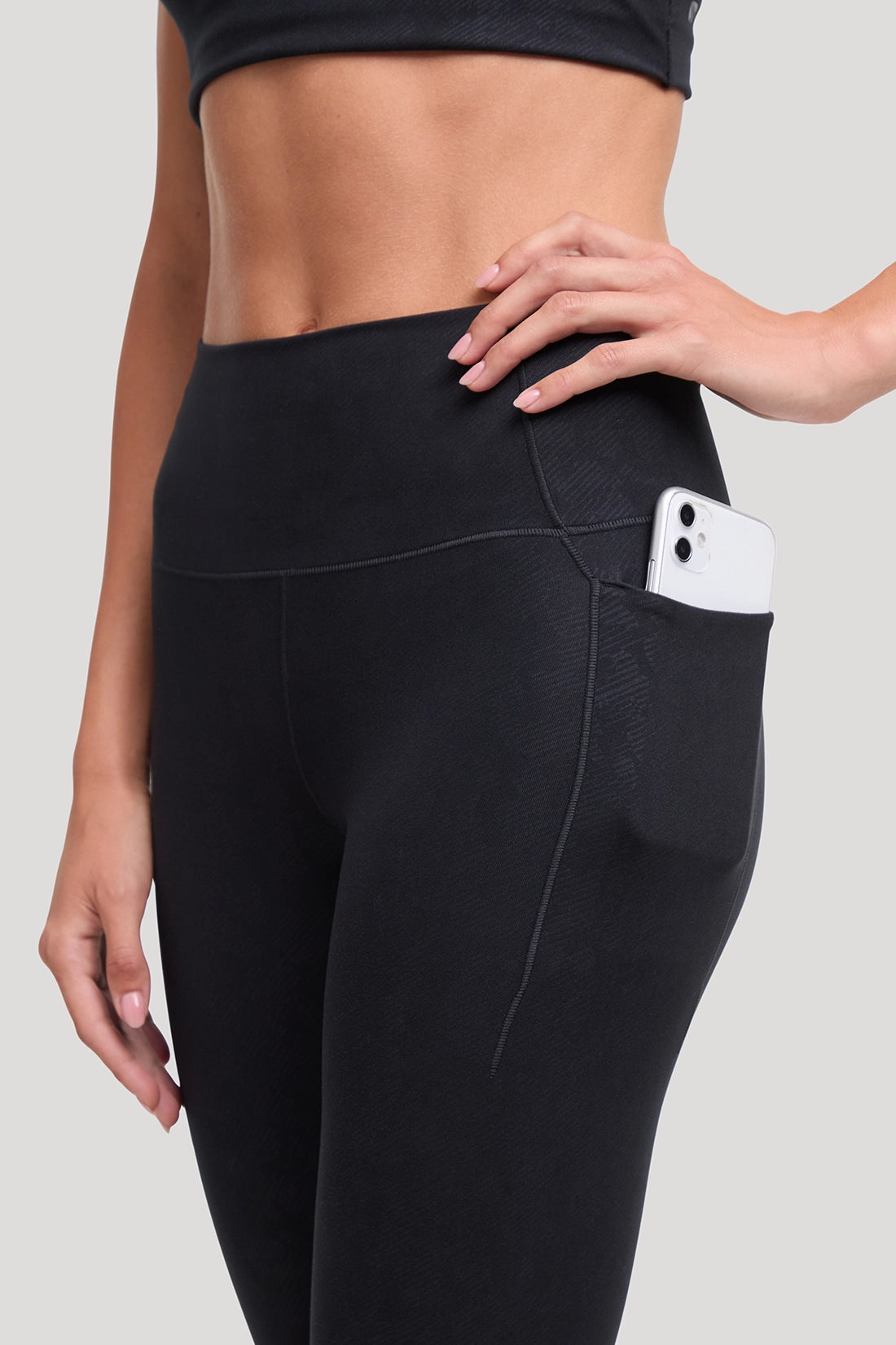 Black high-waisted activewear leggings with all around animal camo print and  with a side pocket holding a white smartphone, shown on a model against a light gray background. #color_black-linear-animal-camo