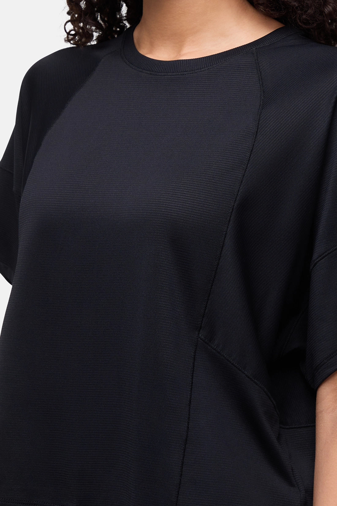Close-up of a person wearing a black short-sleeve top with a crew neck and textured fabric. 