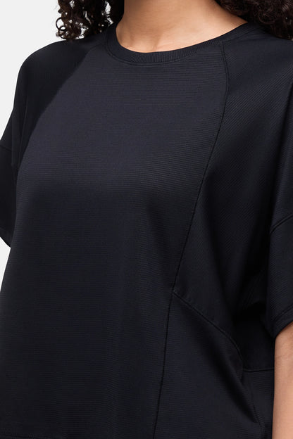 Close-up of a person wearing a black short-sleeve top with a crew neck and textured fabric. 