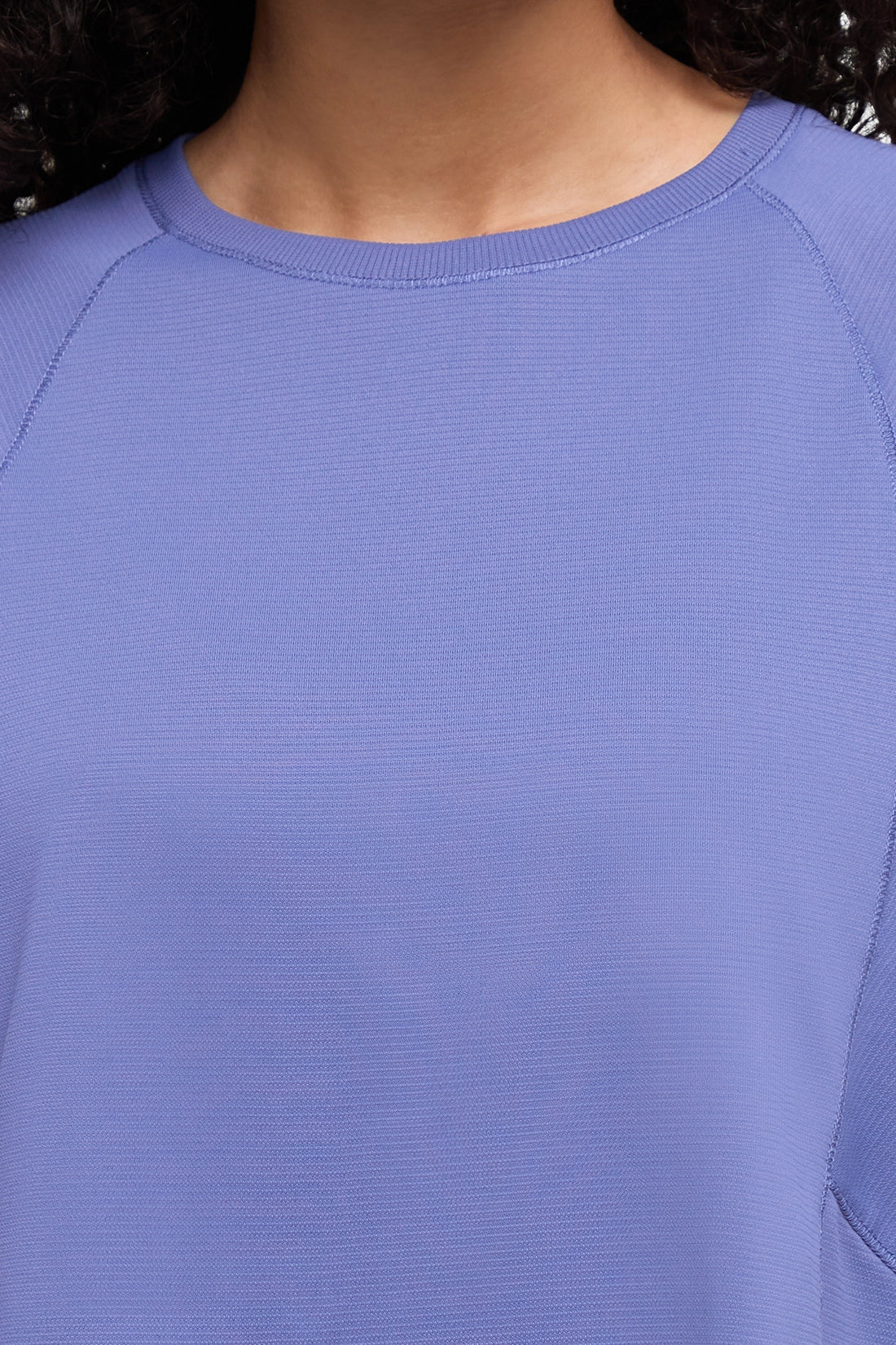 Close-up of a person wearing a ribbed knit top in a periwinkle or light lavender-blue color, showing the crew neck and shoulder area. 