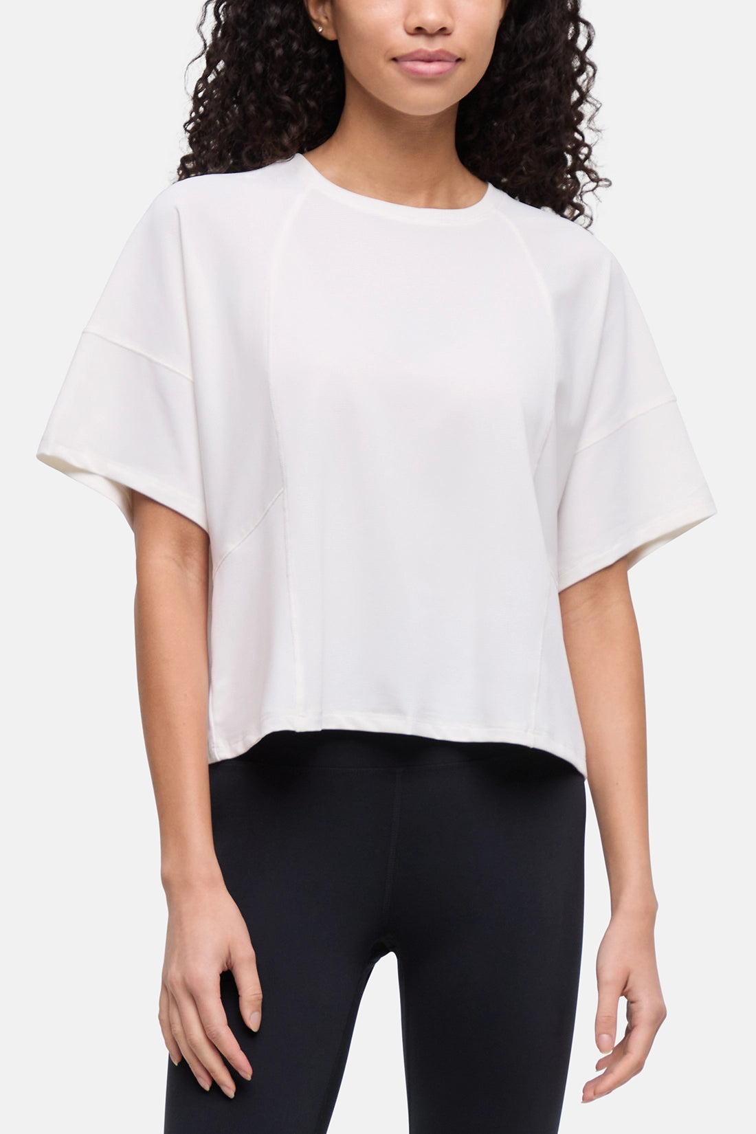 A woman wearing a white short-sleeve crop top with wide sleeves and black leggings, shown from the shoulders to the upper thighs against a plain light background. 
