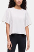 A woman wearing a white short-sleeve crop top with wide sleeves and black leggings, shown from the shoulders to the upper thighs against a plain light background. 