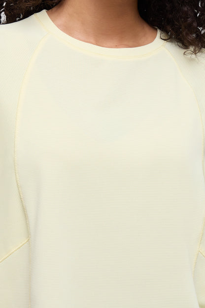 Close-up of a person wearing a pale yellow ribbed long-sleeve top with raglan sleeves and a crew neckline. 