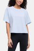 A woman wearing a light blue short-sleeve crop top with side seam details and black leggings, shown against a plain light gray studio background. 