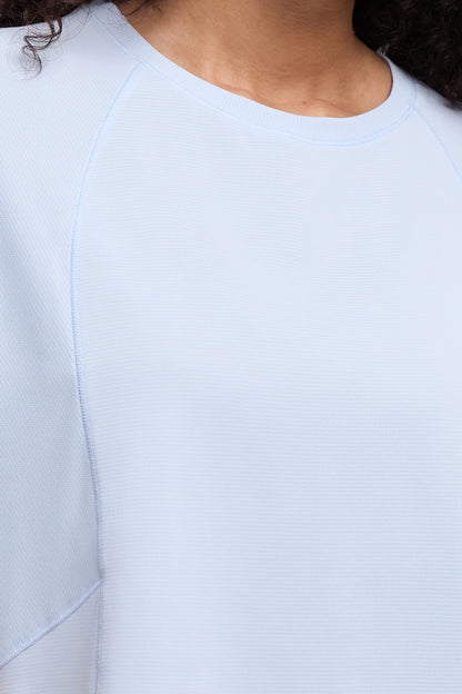 Close-up of a person wearing a light blue ribbed crewneck top, showing the collarbone, neck, and shoulder area. 