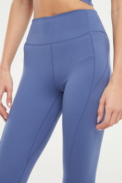 Front close up view of woman wearing blue capris and white sneakers on a light gray background. . 