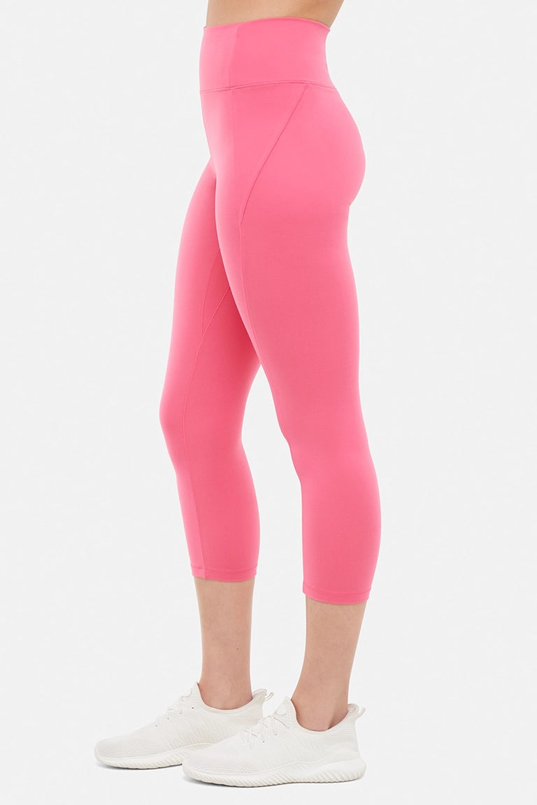 Side view of woman wearing pink capris and white sneakers on a light gray background. 