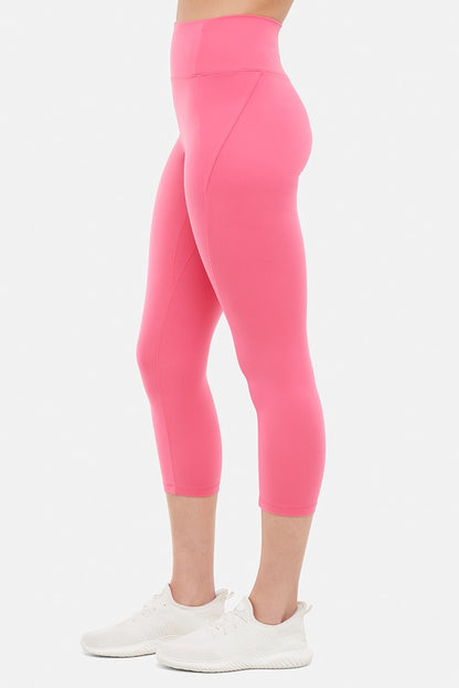 Side view of woman wearing pink capris and white sneakers on a light gray background. 