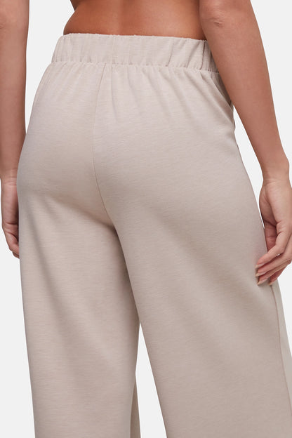 Close-up back view of a person wearing light beige wide-leg lounge pants with an elastic waistband, shown against a plain light gray background. 