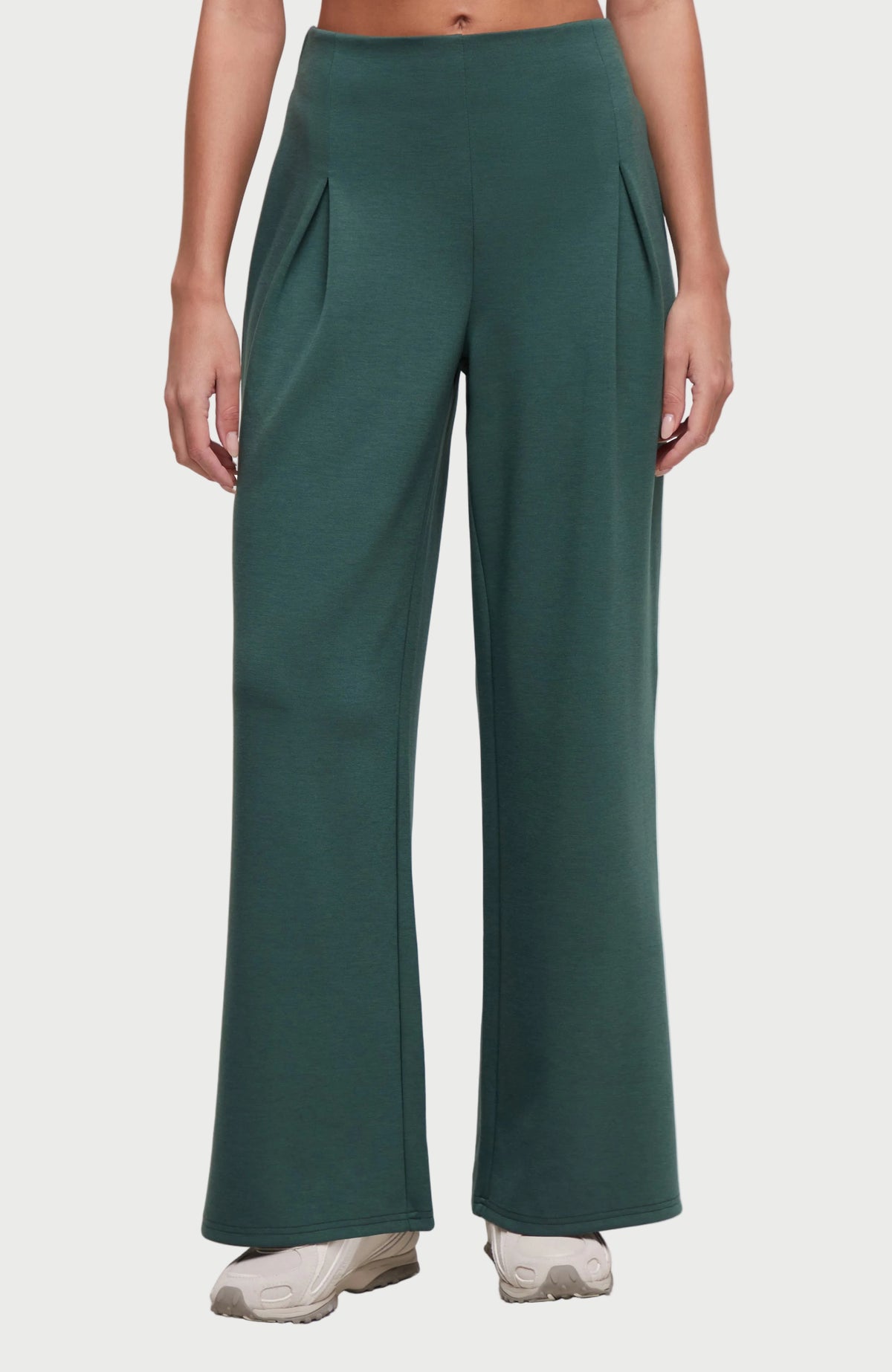 A person wearing dark teal wide-leg pants with front pleat details, paired with light-colored sneakers, shown against a plain white background. 