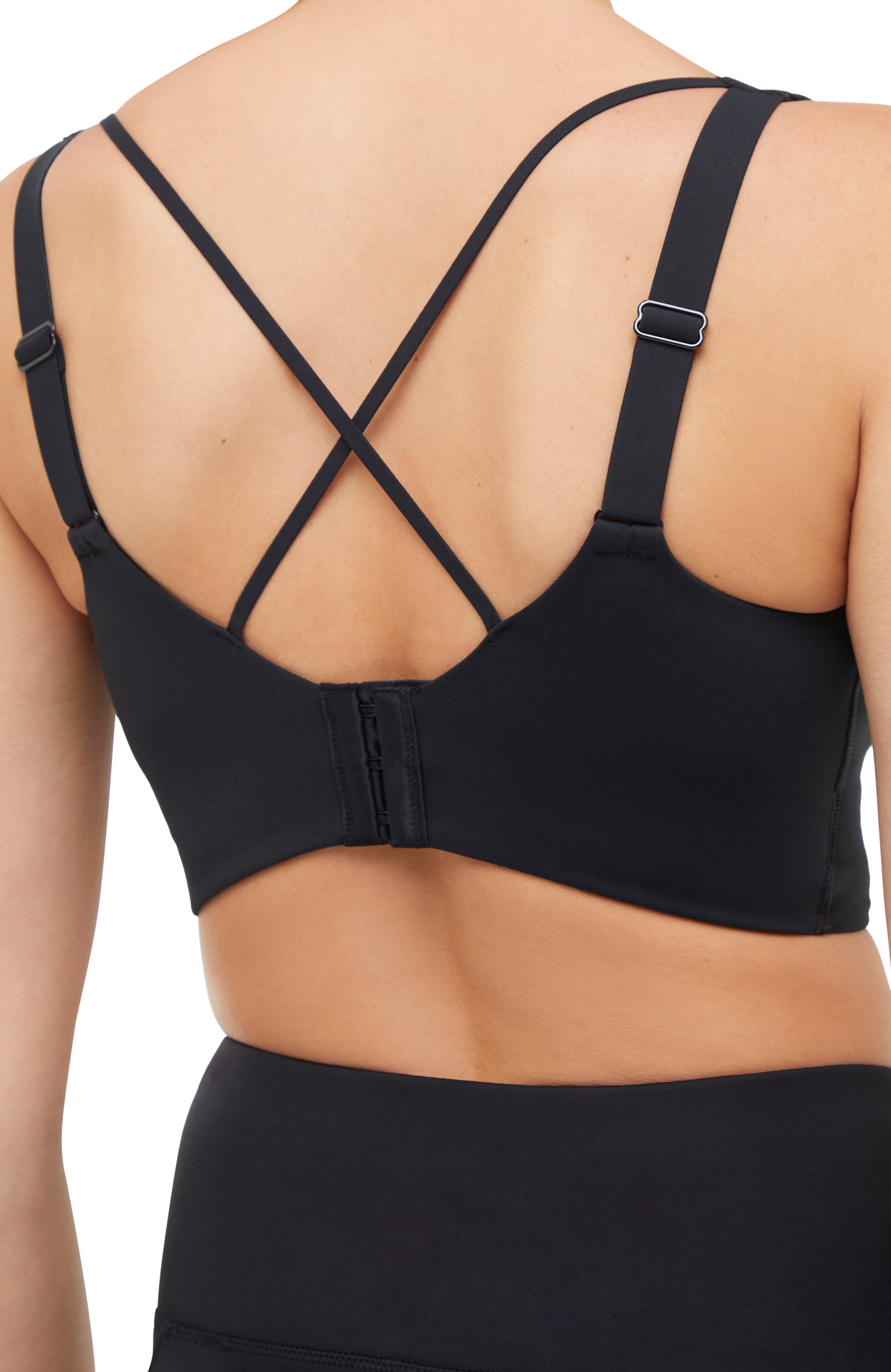 Close up ack of woman wearing a black sports bra and matching black leggings on a white background. 
