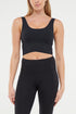 Front view of woman wearing a black sports bra and black leggings on a white background. 