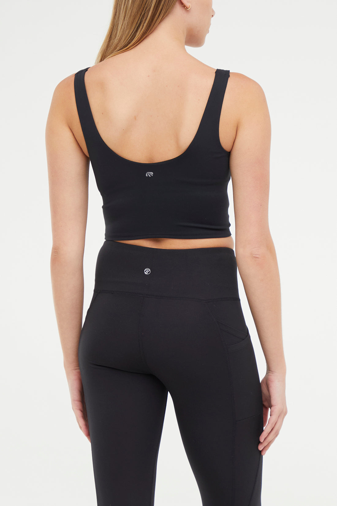 Back view of woman wearing a black sports bra and black leggings on a white background. 