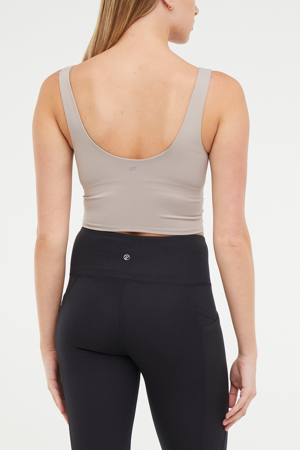 Close up back view of woman wearing a beige sports bra and black leggings on a white background. #color_atmosphere