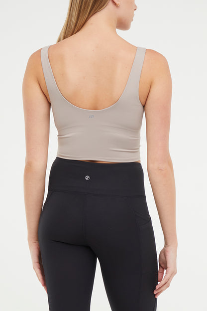 Close up back view of woman wearing a beige sports bra and black leggings on a white background. 